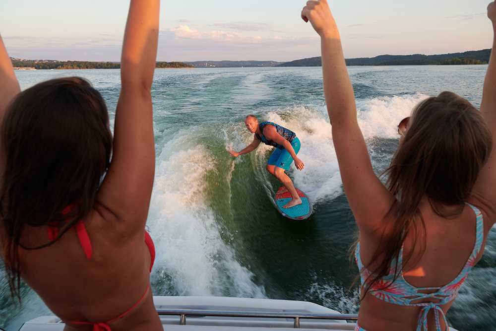 People cheer as a person surfs on the wake of a Cobalt R8 Surf